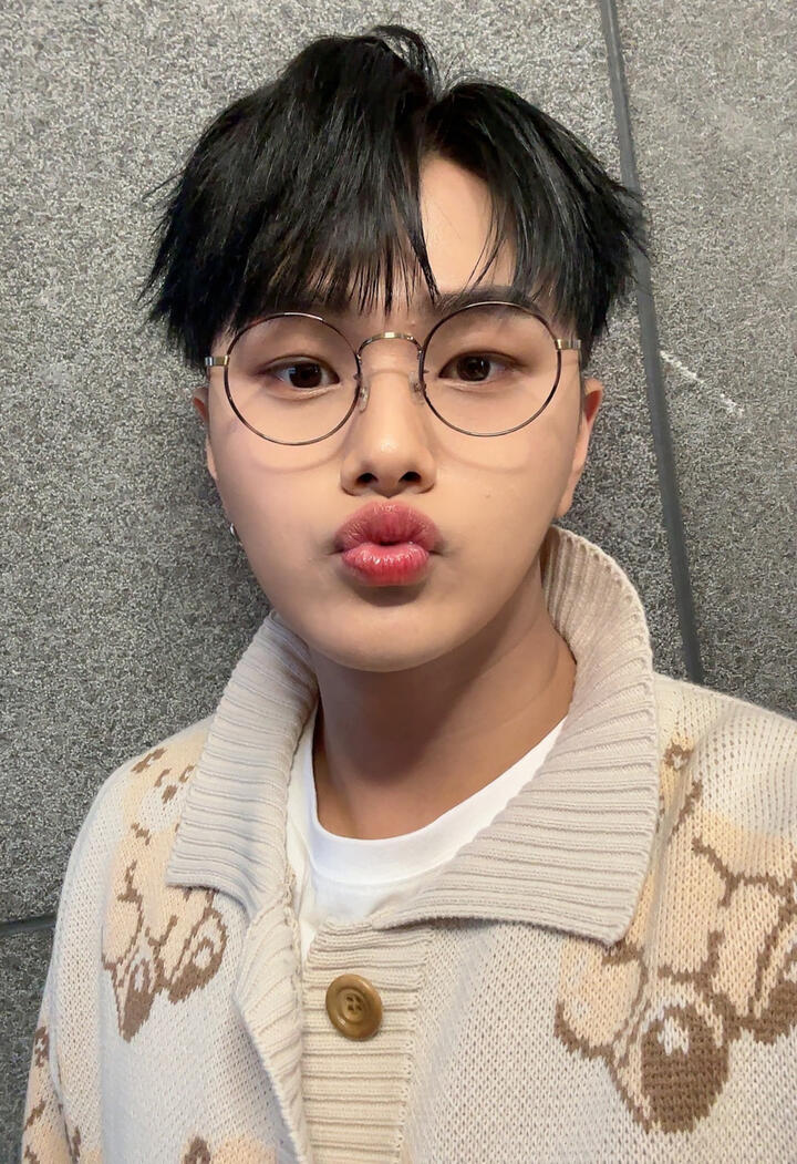 Jahan wearing a bear sweater and thin, wire-frame glasses, and making a duck face at the camera