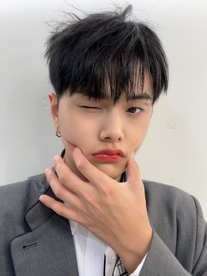 Jahan wearing a school uniform with a cut on his face, pinching his cheeks and winking