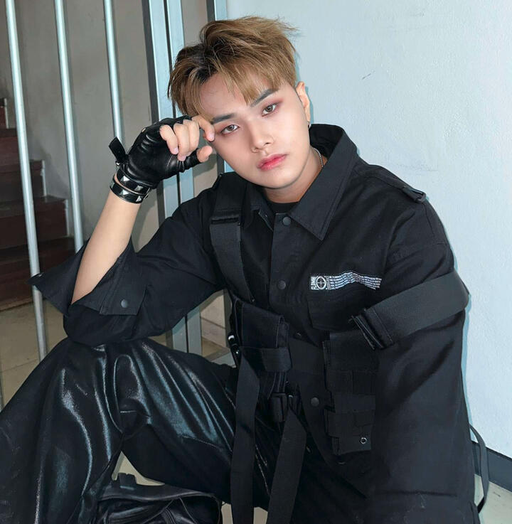 Jahan wearing black techwear, resting his elbow on his knee and head on his hand and looking into the camera