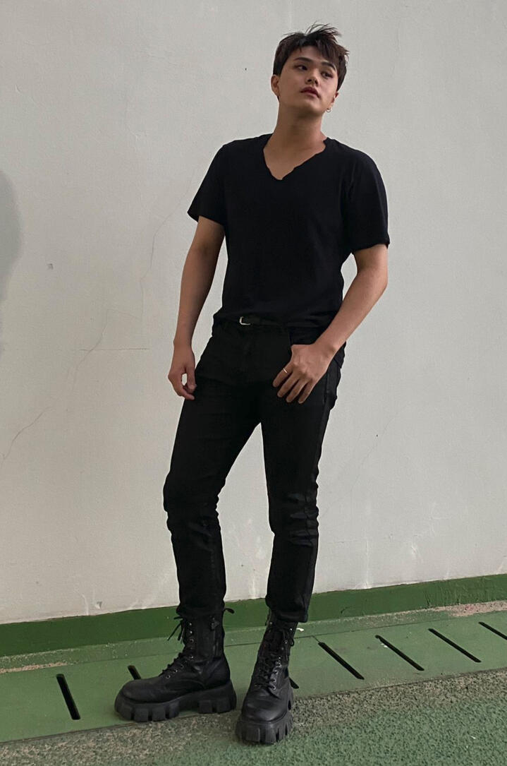 Jahan wearing a black tshirt and black jeans, standing with his hand in his pocket and looking off