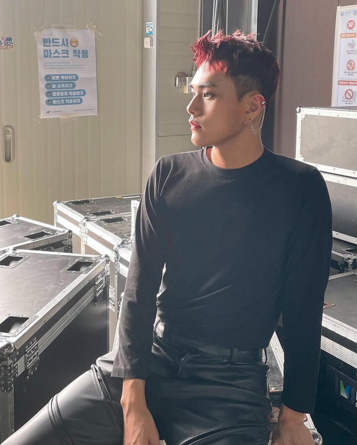 Jahan sitting and wearing a black long sleeve shirt and black pants, backlit and looking to the side