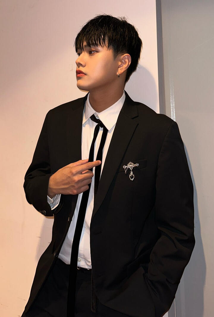 Jahan wearing a suit and lightly holding his tie, looking to the side