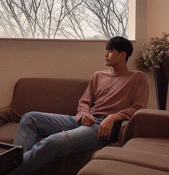 Jahan wearing a pale red sweater and jeans, lounging back on a couch and looking to the side