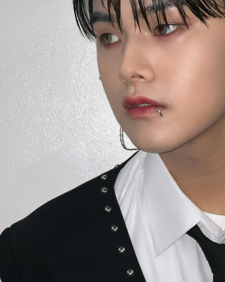 A focus on Jahan's face, he's wearing a studded black jacket over a white button up and a lip ring, gazing off to the side